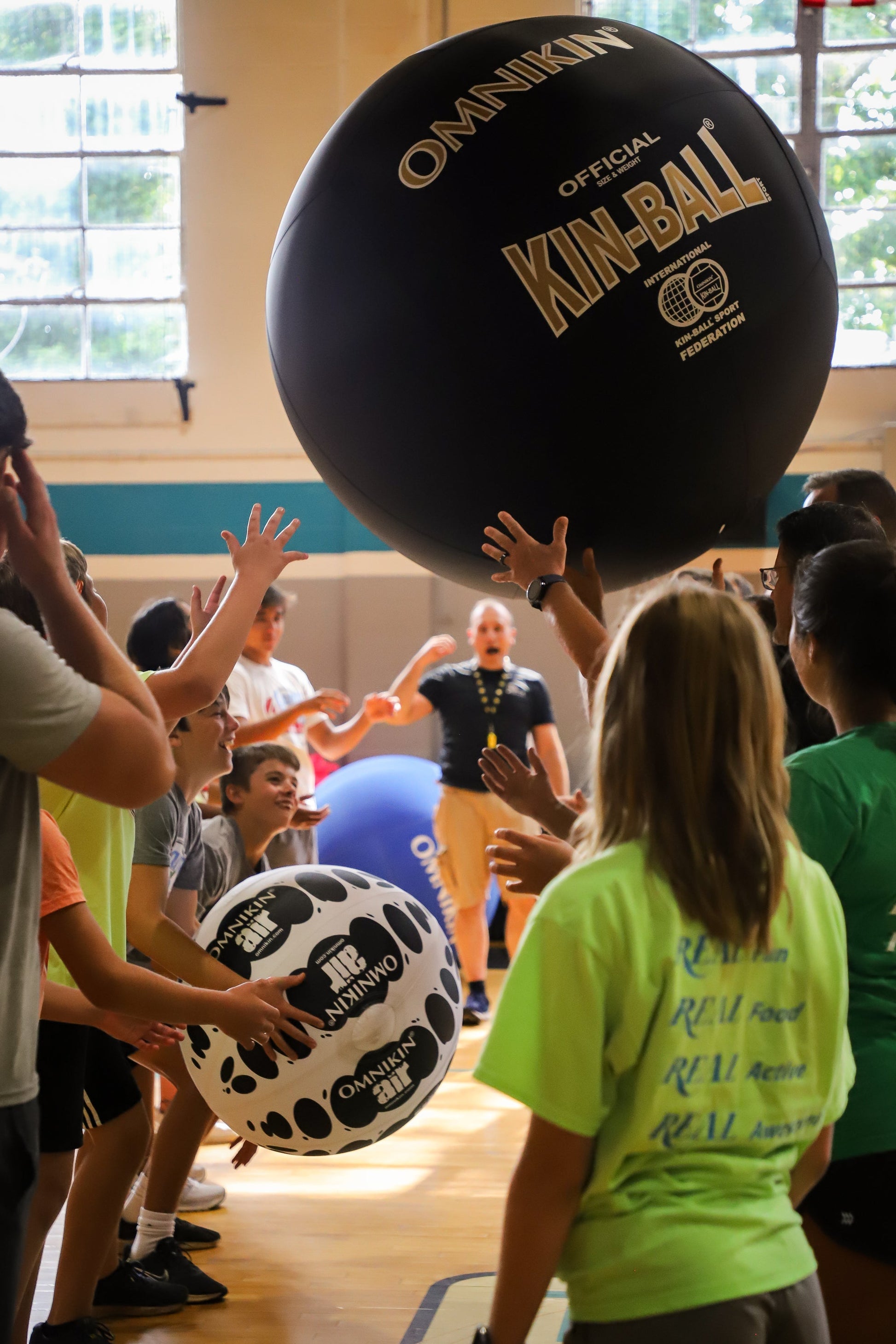 Happy students in a gymnasium playing with a black Omnikin Kin-Ball and black and white Omnikin Air Ball.